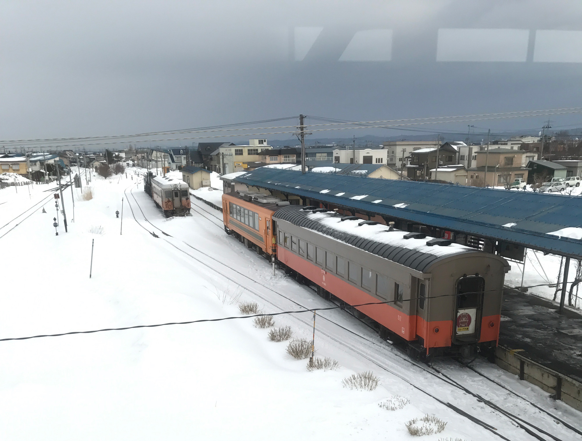 從跨越鐵道的天橋望見橘紅色的暖爐列車，停在一片白雪覆蓋的鐵道上。（攝影／李清志）