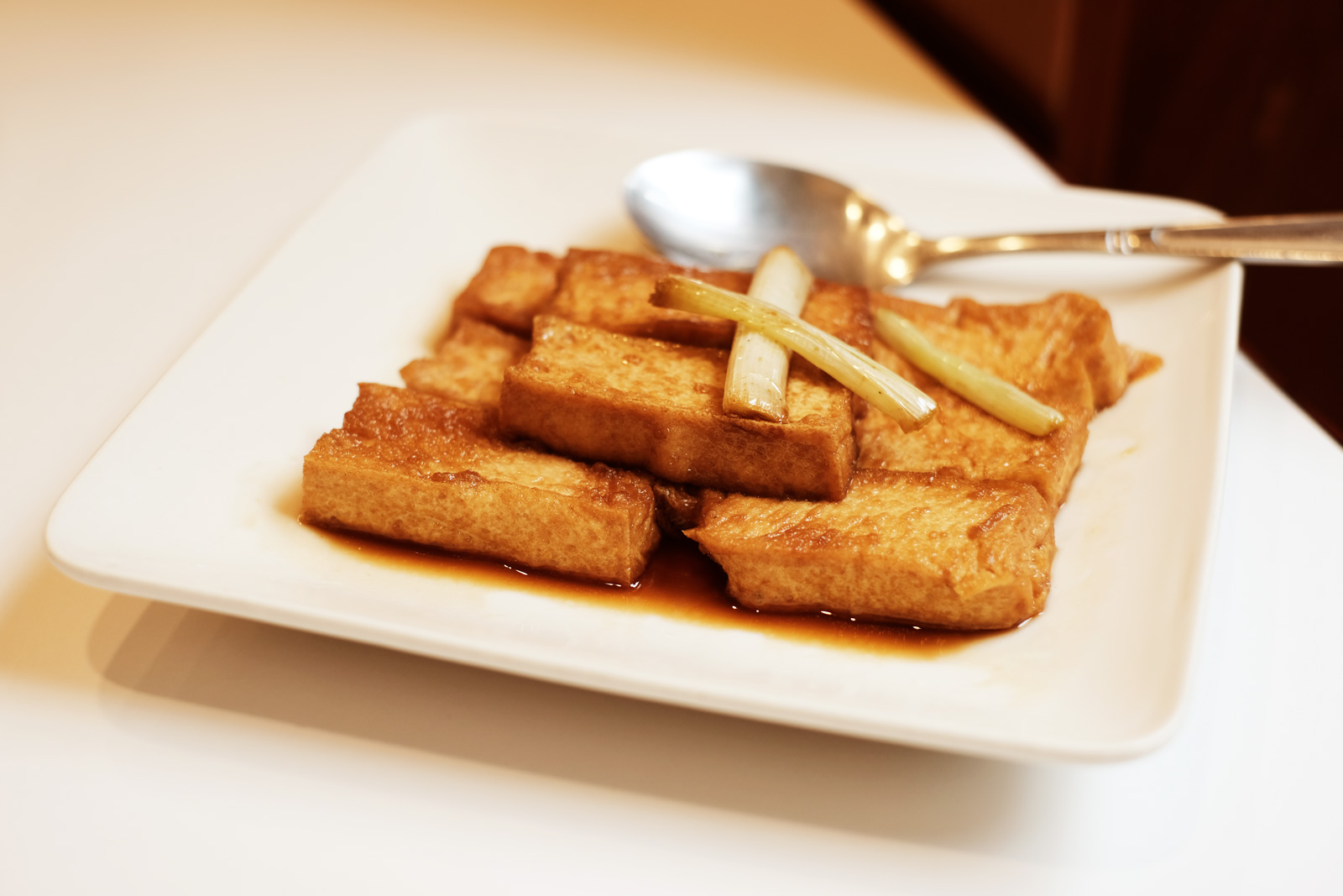 伍佰雞屋的「煎豆腐」，是薄炸過的豆腐，以醬油雞湯煨過，盛盤時，兩截蔥段擱在豆腐上，十分耐吃。（圖片來源：洪愛珠提供）