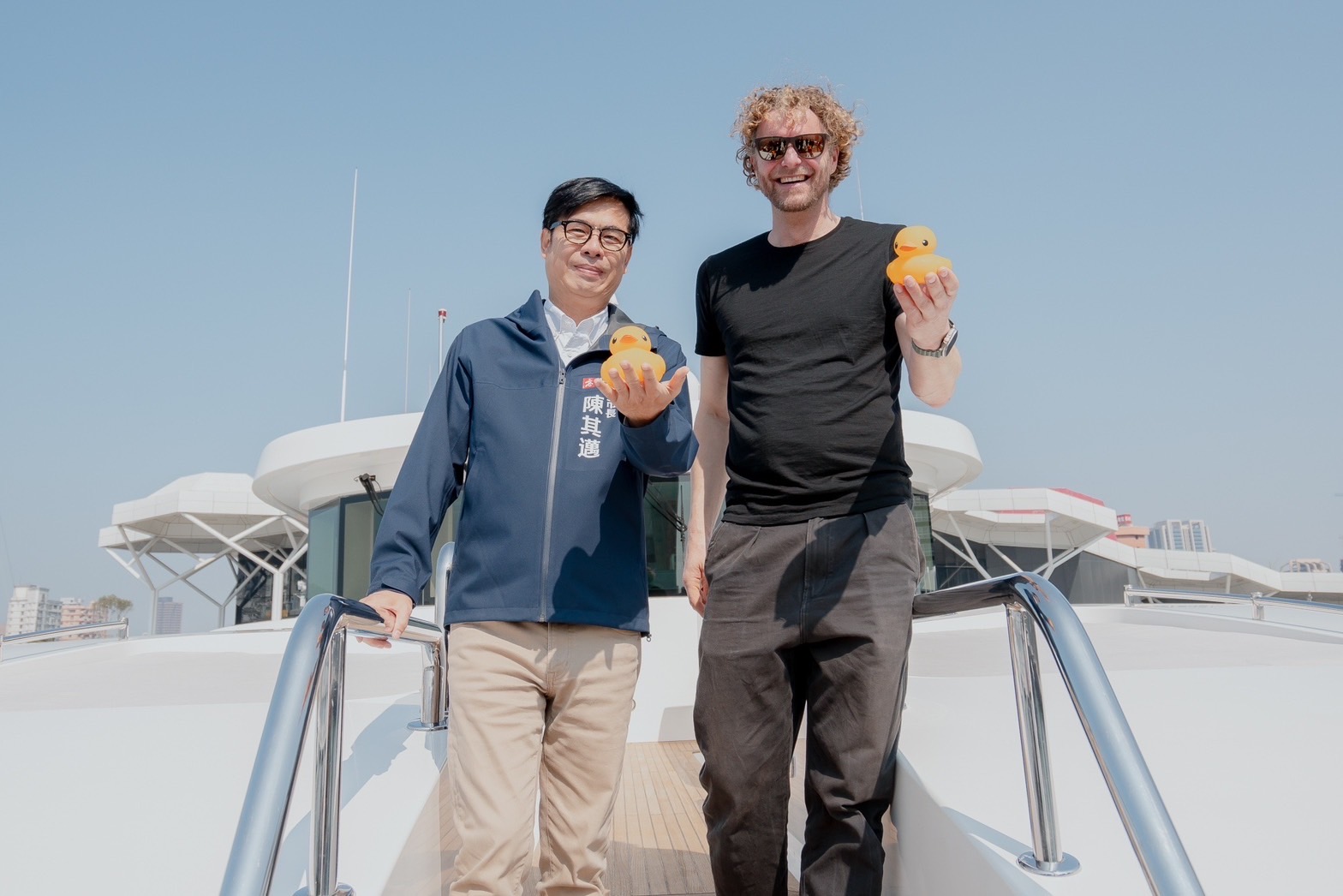 高雄市長陳其邁（左）及荷蘭藝術家霍夫曼（Florentijn Hofman）擔任領航員，搭乘遊艇共同迎接兩隻黃色小鴨入港。（圖片來源：高雄市觀光局）