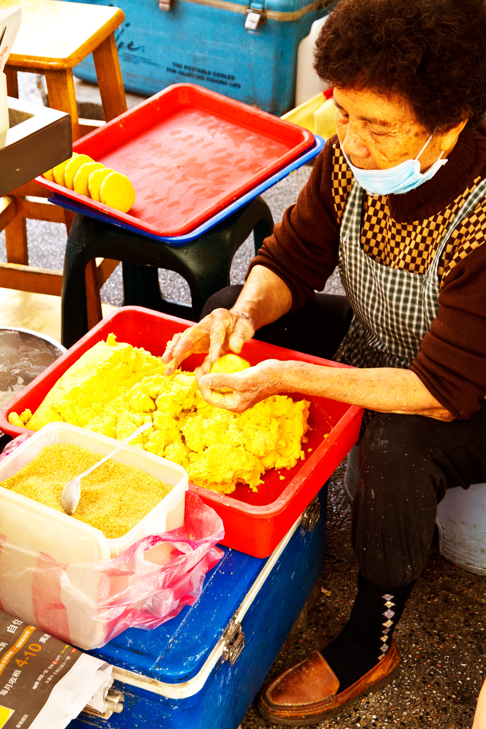 蔡秀蘭阿嬤蹲坐在地上包著番薯椪，用的都是真材實料的黃心地瓜，每天手工現削、現煮，非常費工。（攝影：呂恩賜）