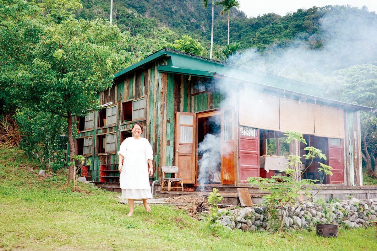 藏在山海之間的木屋，使用回收木料建成，主人李盈慧站在屋前歡迎訪客。（攝影：游琁如）