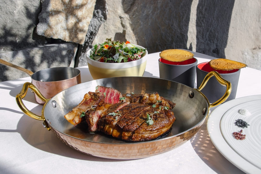 雙人主餐「雲林安格斯黑牛肋眼牛排」為雲林牧場直送肉質軟嫩純淨、毫無腥味。以經典工法煎烤鎖住香氣並充分靜置，成就馥郁迷人的香氣與純粹肉質風味。